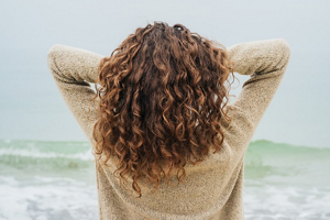 Brunette woman with long curly hair standing in front of the sea